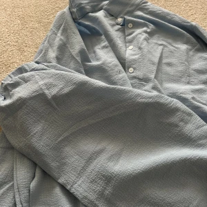 Blått sett - Ljusblått somrigt set med matchade skjorta och byxor.   Vita knappar längs med skjortan.   Endast använd 2-3 gånger, säljer pga att den blivit för liten.   Storlek XS med sitter mer som S då den är oversized.   Nypris: 329kr