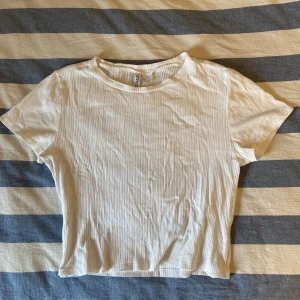 T-shirt Crop-top - Vit kortärmad crop-top från Divido. Nästan helt oanvänd och tidlös. Passar jättebra till en fin kjol, ett par blå jeans eller vad som helst!!
