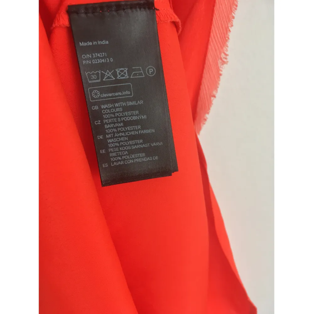 Orange linne i vävt material med råa kanter i chiffong, rundad nederdel. Mått i cm: bröstvidd 46; axelbredd 27; längd fram från axeln 68. . Toppar.