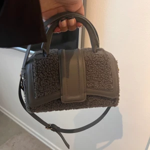 Grå väska  - Mörk grå fluffig väska med band, i nytt skick då den bara är använd 2 gånger 