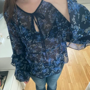 Blommig blus med volangärmar - Så söt blus nu till sommaren! Marinblå med blåa och vita blommor, blusen har även band som knyts framtill