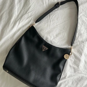 Guess väska svart  - Snygg axelremsväska från Guess. Köpt i Stockholm för ett år sedan och har använt den max 2 ggr. Helt i nyskick! Köptes för ca 2.200kr