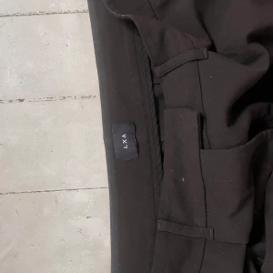 LXA Kostymbyxor - Kostymbyxor från LXA i rak modell, mer oversized i passformen. Dem är mörkbruna i färgen och aldrig använda. Har dock inte prislapp kvar.