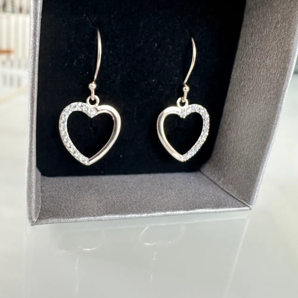 BESKRIVNING  Örhängen i äkta silver i form av hjärtan med små klara Cubic Zirconia stenar upptill. Ett par nätta örhängen med stilren design och skimrig detalj.. Accessoarer.