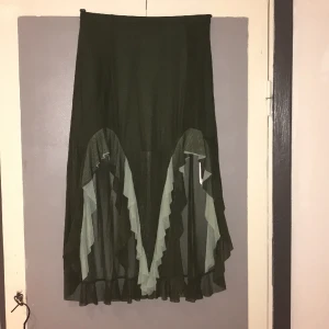 Oanvänd kjol asymmetrisk m resår midja M/38-40 - Oanvänd i material med lite stretch i, resår midjan. Dubbelt tyg ner tills där slits m volang börjar. Perfekt för dans då den fladdrar fint omkring dig. Omkrets midja 70-98 cm höft 103-120, längd 90 cm löngsta delarna fram o bak