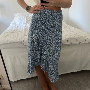 Blommig omlottkjol - En blå omlottkjol med vita blommor. Kjolen har en asymmetrisk fåll och är knälång.💙✨