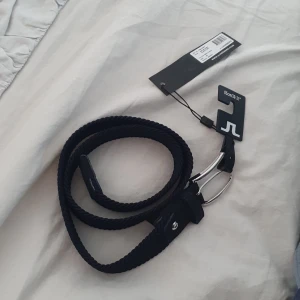 Flätat J.Lindeberg skärp 85 cm - Nytt oanvänt skärp säljes. Längd 85 cm, passar 30-31 midjemått. Mörkblått (nästan svart)