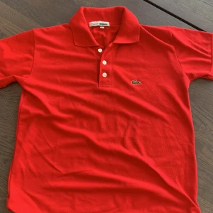 Lacoste Piké - En röd Lacoste piké i ett fint skick! Sizen sitter 1 mindre så den passar för XS.