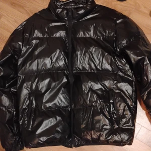 Dunjacka glansig storlek large - Dunjacka storlek large svart, glansig i färgen tjock med inficka samt två fickor dragkedja och knappar