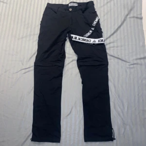 svarta EMP byxor - Svarta byxor med vita och svarta hängslen på ena benet. Byxorna går även att ändra till shorts med en dragkedja. Köptes på EMP för 800.