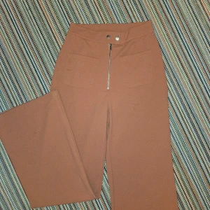 Höjmidjade byxor med dragkedja och fickor fram. - Sköna och stretchinga bygor som är breda i benen. En rosa-orange färg med användbara fickor på framtidan.