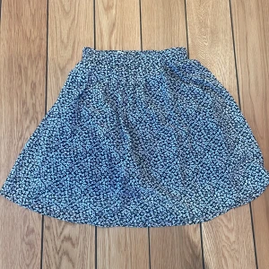 En kort kjol  - En kort svart kjol med vita blommor på i storlek S/M. Denna kjol har används ett fåtal gånger