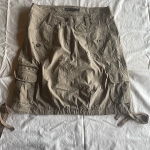 Beige kjol från Soyaconcept - En beige kjol från Soyaconcept med flera fickor och knappar. Kjolen har en justerbar dragsko i nederkanten och är tillverkad i ett slitstarkt material.