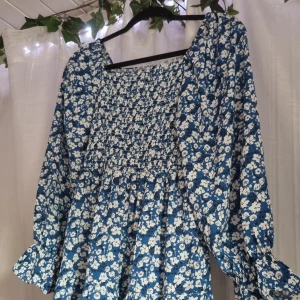 Blommig klänning  - Vit och blå blommig klänning med square neck urrigning. Reså vid armarna somnger en liten fin detalj. Stretch material vid överdelen. Strl. S