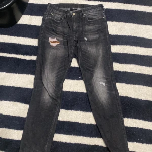 Svarta jeans från Emporio Armani - Ett par svarta jeans från Emporio Armani med slitna detaljer och en broderad logotyp. Jeansen har en normal passform och är tillverkade i denim.