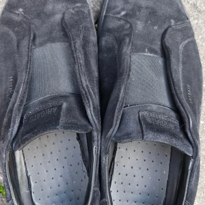 Arigato laceless - Ett par axel arigato laceless i hel svart. Dom är använda en del under 6 månader. Har tyvärr ingen låda men har en dustbag till den. Skroan ahr inga större skador men dom är lite smutsiga men det är väldigt lätt att ta bort, speciellt på sulan.