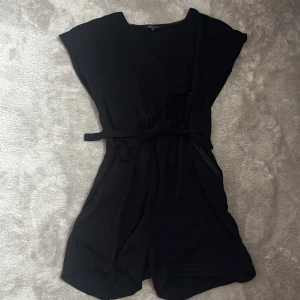 Klänning med shorts  - Svart ”klänning” med shorts. Knytning i midjan som går att ta bort. Knapp vid brösten. 