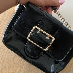 Lackad väska - Svart lackad axelremsväska med guldfärgat spänne från Dorothy Perkins. Säljes i begagnat skick. Inuti finns ett blixtlåsfack. 💘