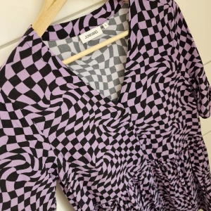 Klänning (Nyskick) Strl S - Klänning  Strl S Nyskick! Färg: Lila, Svart Junkyard  Supersnygg klänning i retro-stil. Grafiskt mönster, lite Y2K! Sval och skön kvalitet. Rak, lite vidare modell. Knappar fram. Endast använd en gång!