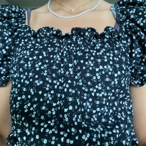Svart topp Gina Young  - Denna topp/blus är svart med puffiga ärmar och vita blommor 🌸 Superfin till sommaren! Har endast använts några gånger och är därför i väldigt bra skick, säljer den eftersom att den är lite kort på mig 