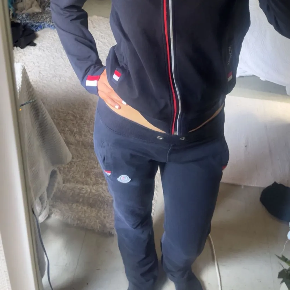 En supersnygg tracksuit/mjukisset. En mörkblå munkjacka med dragkedja framtill och röd-vit randig detalj längs dragkedjan. Hoodien har långa ärmar och Monclers logotyp på bröstet. Mörkblå mjukis byxor med lågmidja och som är . Tröjor & Koftor.