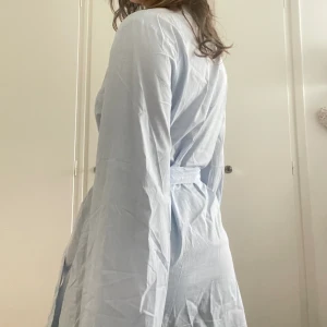 Blå morgonrock - En superluftig och skön morgonrock i ett ”skjort-aktigt” material, perfekt till sommaren!💕 Kollar man närmre så är den lite vit- och blårandig. Den är i storlek S och man kan spänna in och ut midjesnöret!🫶🏼