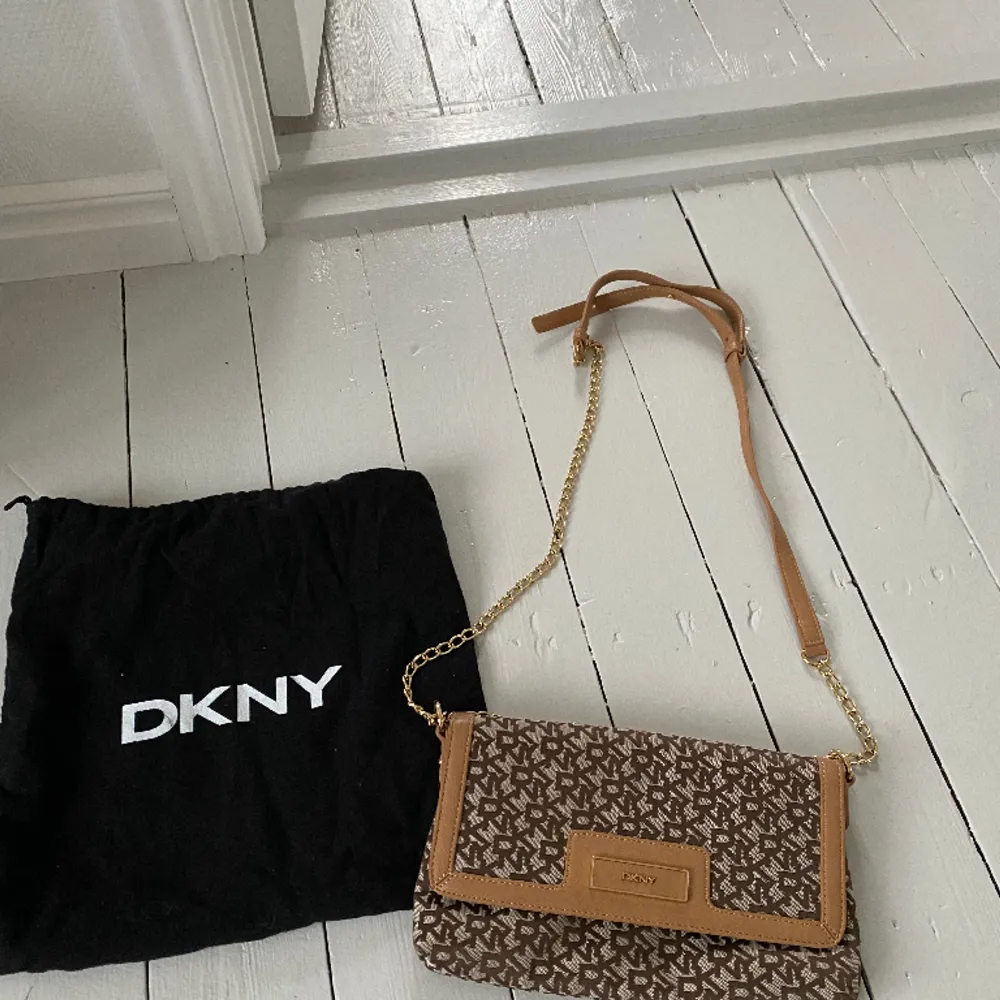 Helt ny DKNY handväska i brunt/beige skinn och beige tyg. Justerbar axelrem så väskan kan bäras cross body eller på ena axeln. Fack med dragkedja inne samt två mindre fack förutom större.  Svart dust bag medföljer. Nypris ca 1500 kr. . Väskor.