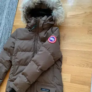 En brun parka från Canada goose i stl XS. Jackan är i en äldre modell men är väldigt sparsamt använd då jag snabbt växte ur den.  Jag skickar gärna fler bilder om så önskas!  Kan mötas upp för överlämning i Uppsala. 