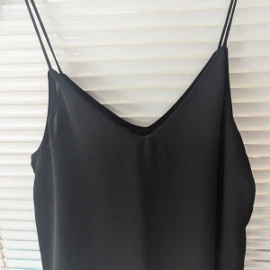 Svart elegant linne med tunna axelband från Zara,M - Ett elegant svart linne med tunna axelband och v-ringning. Linnet är tillverkat i ett lätt och luftigt material, perfekt för varma sommardagar eller som ett lager under en kavaj.Strl M, men det passar perfekt till S också. Mycket fint skick.