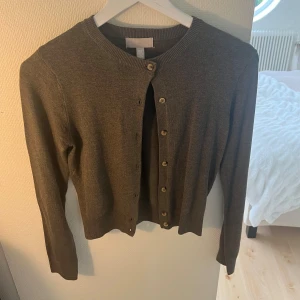 Brun kofta - En brun kofta med långa ärmar och knappar framtill. Koftan har en rund halsringning och är tillverkad i ett mjukt material.