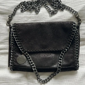 Stella Mccartney liknande väska - Säljer min superfina väska som liknar Stella Mccartneys väskor. Bandet går att ta av om man vill det. Den är sparsamt använd och har bara tappat lite färg på den lilla kedjan som sitter ihop med den runda detaljen (bild finns)🥰