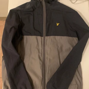 Lyle & Scott Vindjacka Herr M - Snygg grå/svart vindjacka från Lyle & Scott. Fint skick och perfekt som vårjacka då den är ganska tunn men vindavvisande. Medium. Säljs antingen med frakt där köparen betalar frakten alternativt mötas upp i Stockholm.  Mvh Mathias