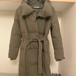 Jacka med bälte - Lång Jacka från Chelsea i mörkgrön med bälte och knappar. Använt 2 gånger. Inga fläckar. Väldigt varm och skön