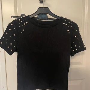 T-shirt med pärlor  - Svart t-shirt med pärlor på axlarna. Ribbat material. Använd några få gånger o är i fint skick. 