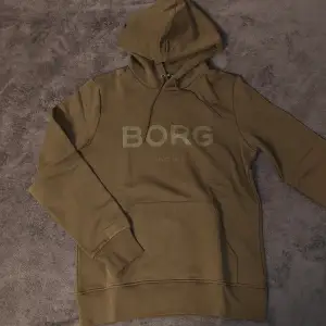 Mörkgrön/olivgrön Björn Borg hoodie i storlek large. Skönt material och varm med bra passform. Säljer då den inte är min stil längre. Helt oanvänd. Skriv vid minsta fundering eller för fler bilder!