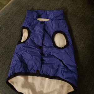 Blå hundjacka  - Ca 40cm i ryggmått. Insida i plysch, stängs med tryckknappar. Aldrig använd, men har blivit tvättad.