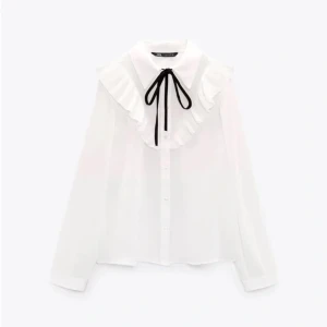 Zara vit blus  - Vit zara blus med svarta knyten vid kragen och volanger, i nyskick. 