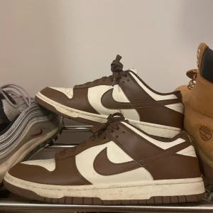 NIKE DUNK LOW - Ett par nike dunk low cocoa i storlek 42. Måttligt använda men fortfarande i bra skick. Köpt på sneakershyllan i stockholm. Inget kvitto samt behöver pengarna relativt fort därav priset. Tveka inte att skriva om du skulle ha några frågor