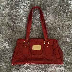 Skimrande vinröd vintage väska ❤️✨ - Säljer nu denna super fina väska från dolce& gabbana. Den är köpt i en secondhandbutik i Italien därför orsärker om det ör äkta. Väskan har ett lite plastig material!  Skicket är inte som ny då den är vintage.  Bred: 37cm längd: 20cm