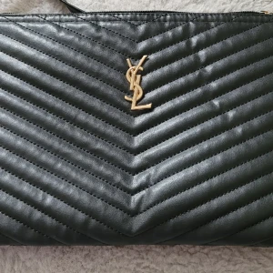 Fejk handväska  - Säljer en fejk ysl handväska i svart fejkläder, med rutit innertyg, med en liten ficka på insidan med dragkedja