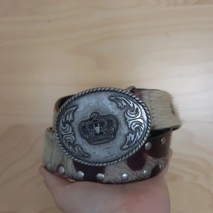 Ett cowboy/western skärp med nitar och spänne - Skärpet imoterar koskinn och nitar, är 85 cm långt och har ett spänne med en krona på.
