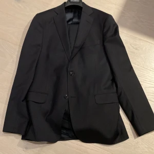 Slim kostym Oscar Jacobson stl 152 i navy - Slim kostym från Oscar Jacobson Kavaj Edmund och Byxa Damien Storlek 152 (innebenslängd 78 byxa och längd kavaj bak 78 cm) Färg Navy Material: 60 ull/ 35 pes/ 3 elastan/ 2 nylon  Mycket gott skick, använd 3 ggr Nypris 6000 sek 