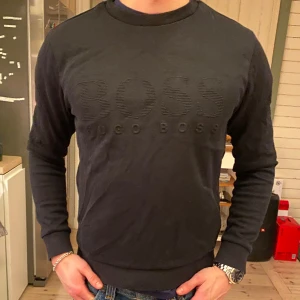 Hugo Boss Crewneck, svart - Hugo Boss crewneck, slim fit, storlek S. I väldigt bra skick men är lite skadad på högra samt vänstra ärmen, men syns inte!