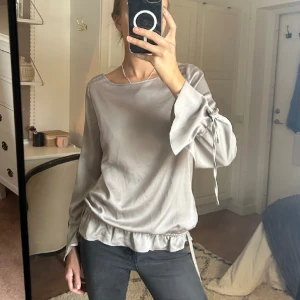 Blus från Monari - Säljer denna blus från Monari. Aldrig använd med prislapp kvar. Knytningar vid armarna och längst ner samt söta strassdetaljer på axlarna!