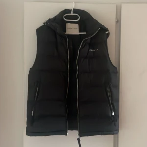 GANT väst (avtagbar luva)  - Använd 2 gånger, helt i nyskick. Luvan går att ta av om man vill. 2 stora ytterfickor med dragkedja och 3 innerfickor varav en med dragkedja. Köpt för 2 500 (finns bild i annonsen) 