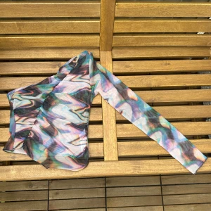 Asymmetrisk och unik mesh topp i storlek 38 (S/M) - En färgglad och häftig party topp med en ärm! Använd 1 gång. Köpt från Asos. Mycket stretch i tyget och sitter som storlek S-M.
