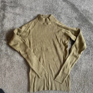 Beige ribbad polotröja - En olivgrön ribbad polotröja med långa ärmar. Tröjan är tillverkad i ett stickat material och har en hög krage.