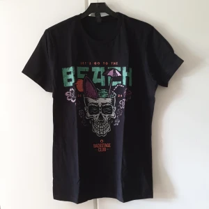 Ny svart dödskalle T-shirt, EMP backstage club  - T-shirt,  Storlek: uppskattas som M/L (står L på lappen)  Skick: ny, endast provad  Färg: svart med dödskalle och text "let't go to the Beach" Märke: EMP Backstage club Längd: ca 65cm, axelbredd: ca 40cm 
