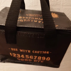 Ouija lunchlåda kylväska med dragkedja  - En jättesöt lunchlåda med ouijabräde motiv utanpå. Svart med silver insida. 