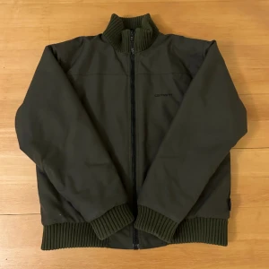 Mörkgrön Carhartt jacka  - Vintage Cordura plus Carhartt jacka i mörkgrön färg. Mycket hållbart material, innerficka, quiltad innersida.  Osäker på storlek pga att texten på tvättlappen gnuggats bort men borde vara Medium
